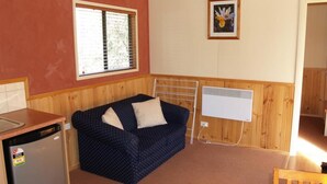A small, cozy room with a kitchenette, a window with blinds, a radiator, and a framed picture on the wall. - Launceston Holiday Park Legana (Legana)