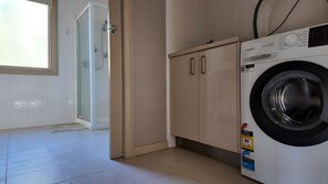 A laundry room with a Westinghouse washing machine, a glass shower enclosure, and a door leading to a bathroom. - Launceston Holiday Park Legana (Legana)