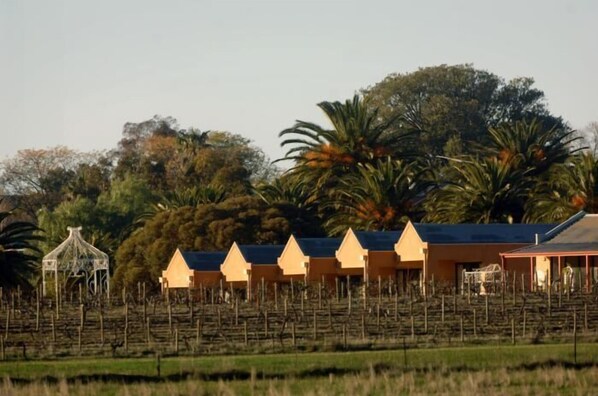 A row of yellow-roofed buildings with a gazebo in front, surrounded by trees and a fence. - Tuileries (Rutherglen)