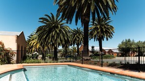 Piscina con palmeras y una valla, rodeada de edificios.