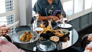 Una mesa redonda para comer con diversos platos, copas de vino y un florero con flores.