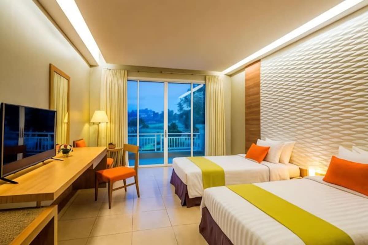 A hotel room with two beds, a desk, a chair, a TV, and a balcony with a view.
