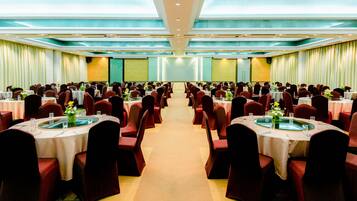 A banquet hall with round tables and red chairs, arranged in rows.
