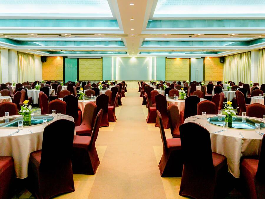 A banquet hall with round tables and red chairs, arranged in rows.