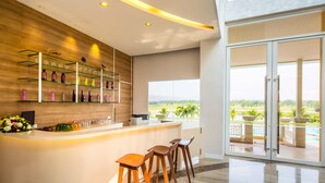 A modern bar area with a wooden backdrop, glass shelves, and a view of a landscaped area through large glass doors. - Pattana Sports Resort (Si Racha)