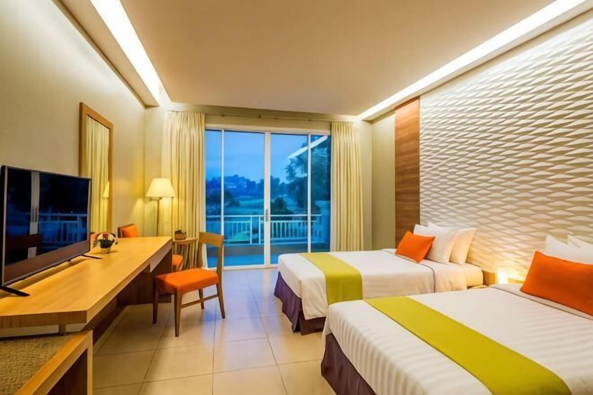 Quarto de hotel com duas camas, uma escrivaninha, uma cadeira, uma televisão e varanda com vista.