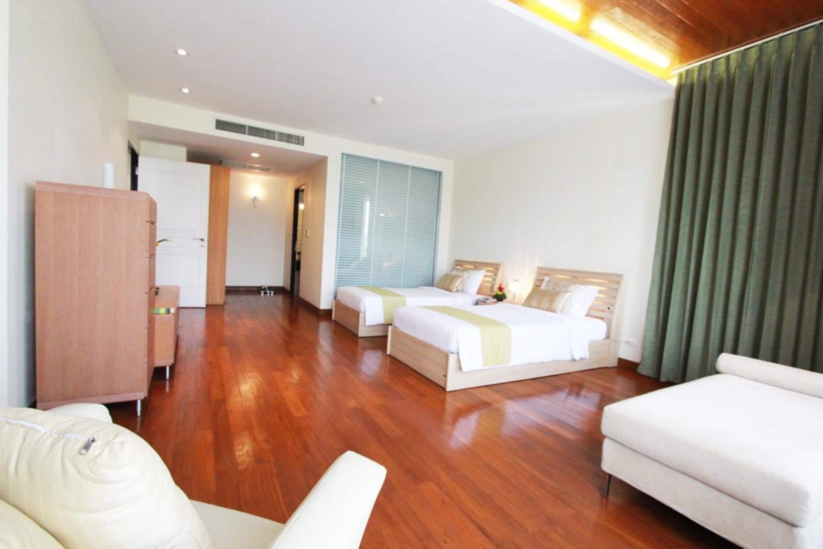 Una habitación de hotel con dos camas, un armario de madera, un sofá y un ventanal con cortinas.