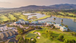 A golf course with a large building complex, multiple water bodies, and surrounding hills. - Pattana Sports Resort (Si Racha)