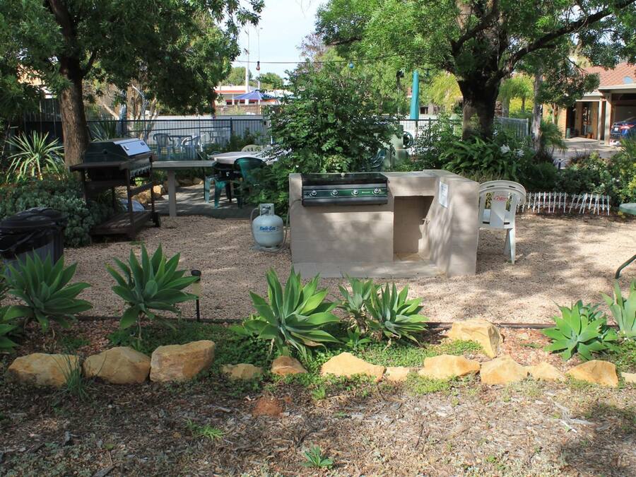 Un patio trasero con una parrilla, una estación de asado y un espacio de descanso con sillas.