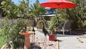 A patio area with a red umbrella, a bird sculpture, a swan sculpture, and a potted plant. - Orana Motor Inn (Irymple)