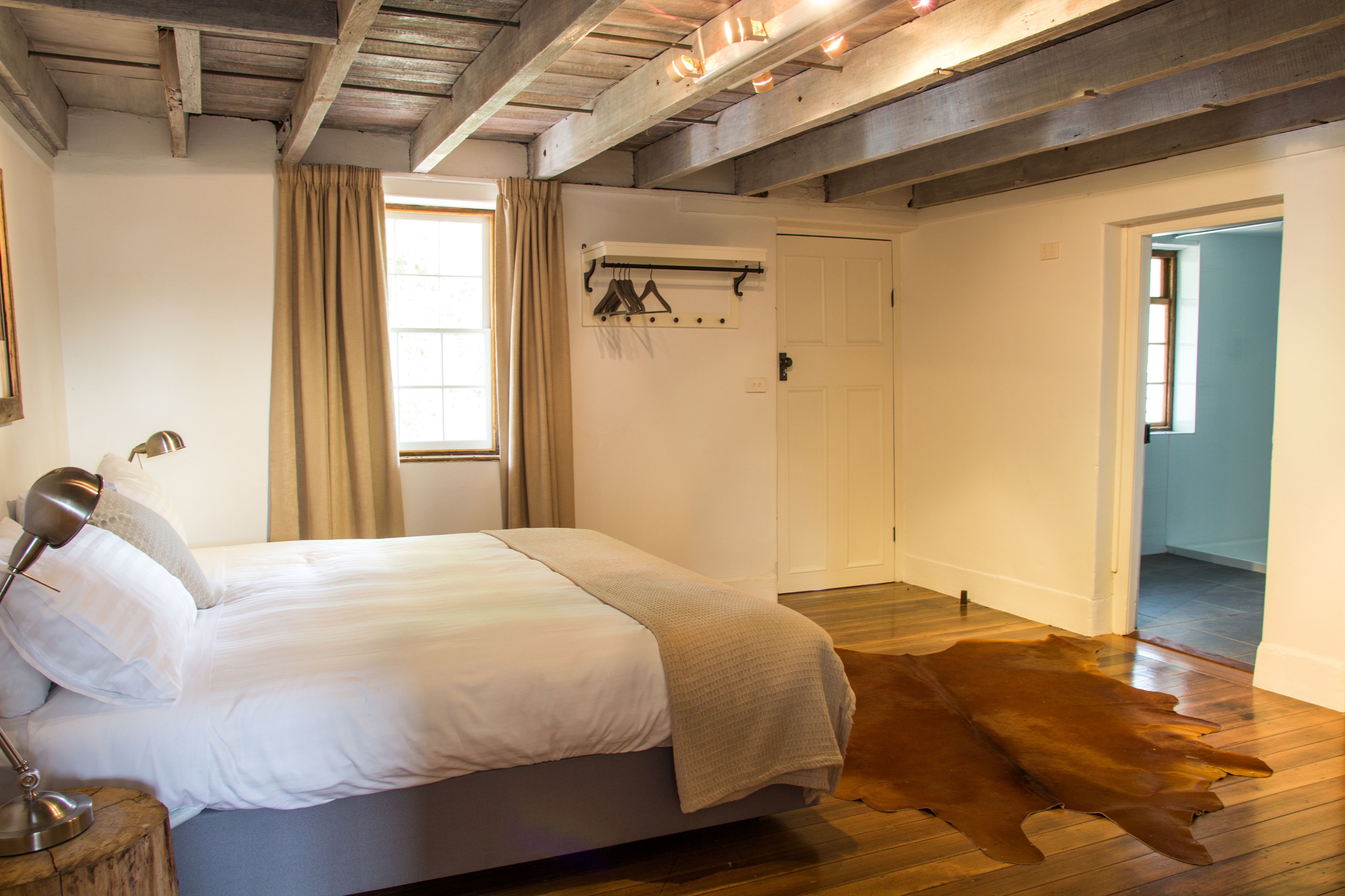 A bedroom with a bed, a wooden floor, a hanging coat rack, and a door leading to another room.
