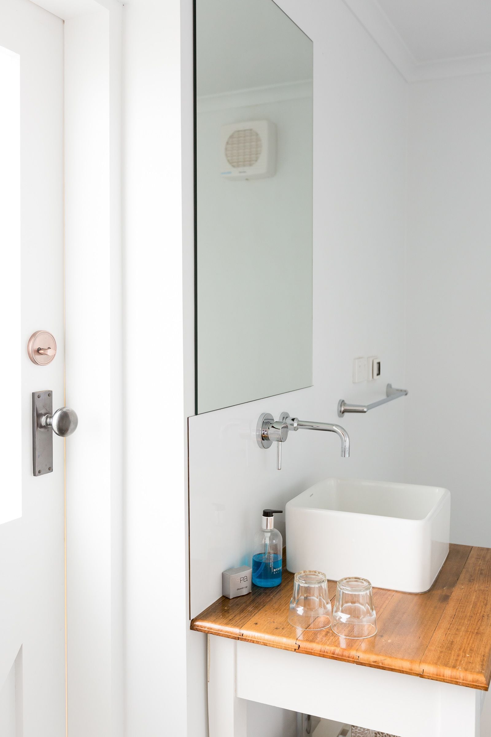 A bathroom with a white sink, a mirror, a shower, and a door with a round handle.