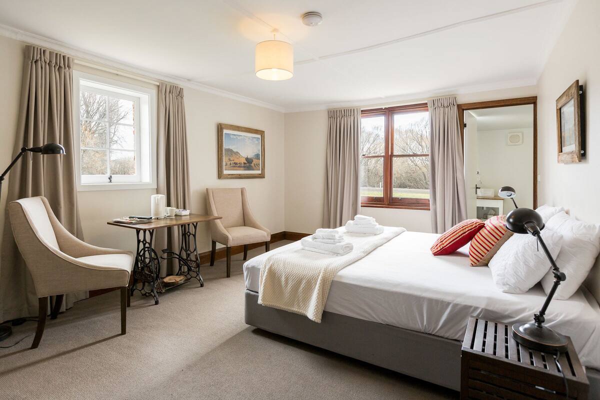 A hotel room with a bed, a desk, a chair, a lamp, and a window with curtains.