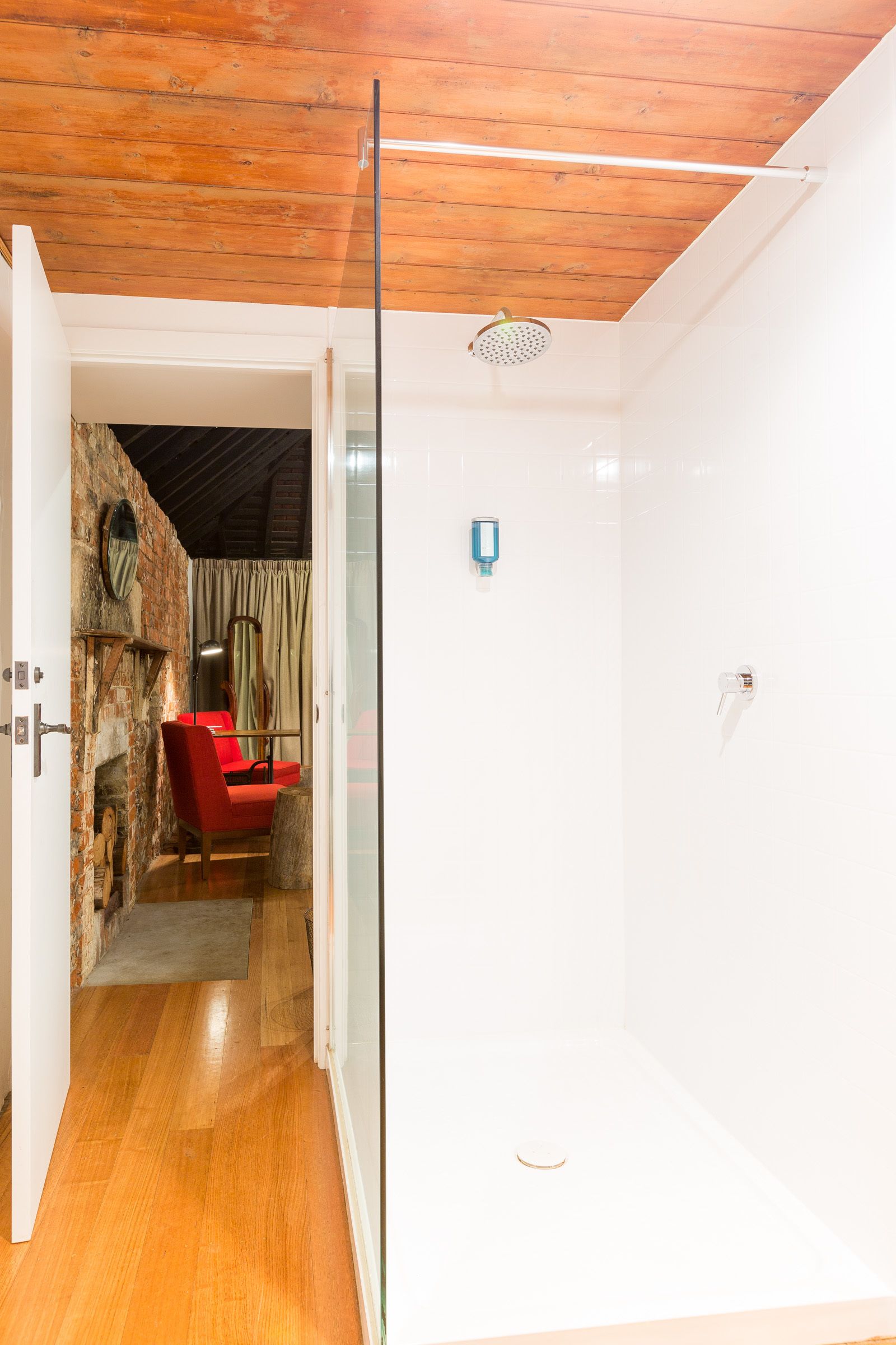 Una habitación con techo de madera, cabina de ducha de vidrio, una silla roja y pared de piedra.