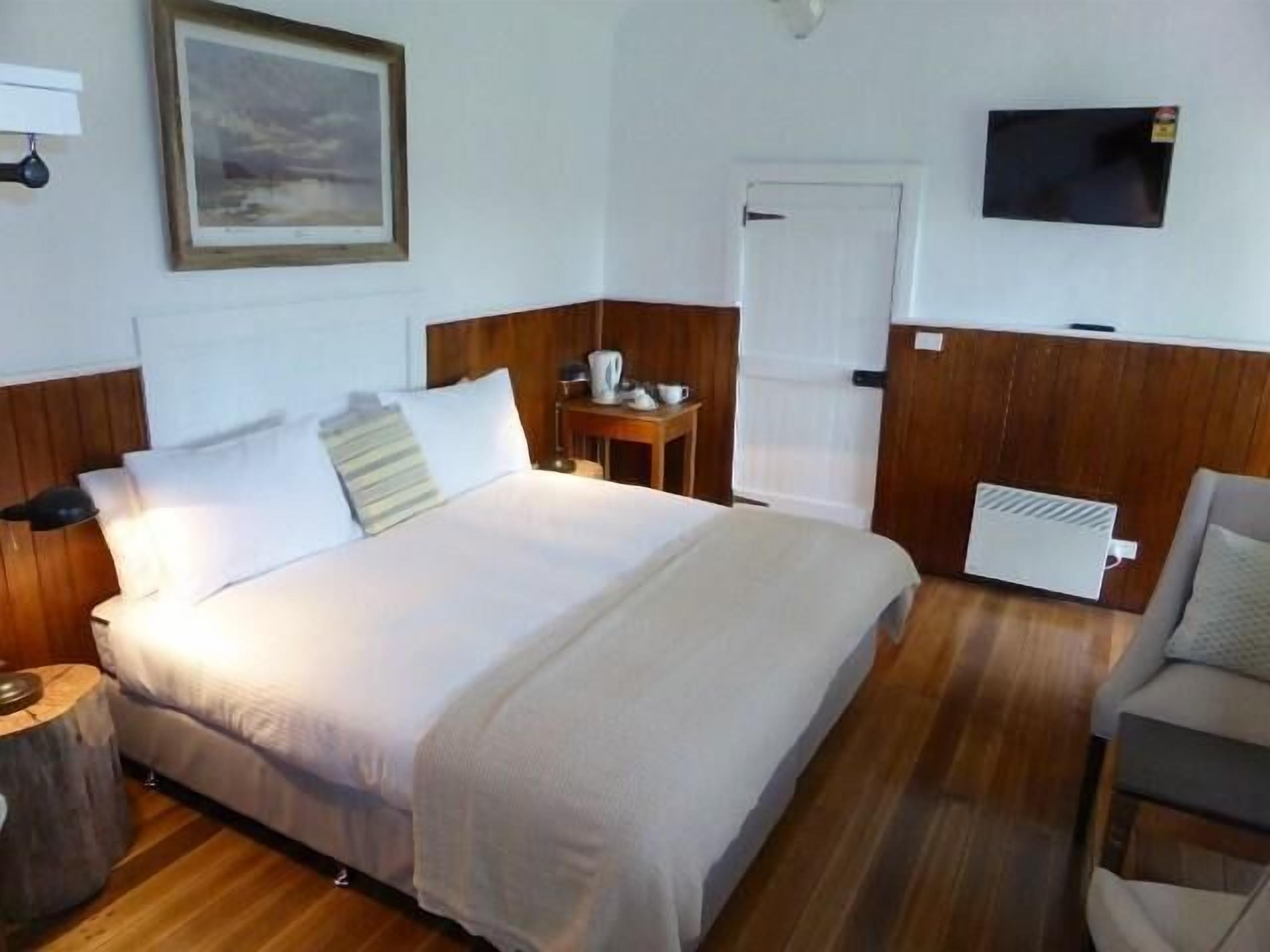 A neatly arranged hotel room with a bed, bedside table, chair, and a television mounted on the wall.