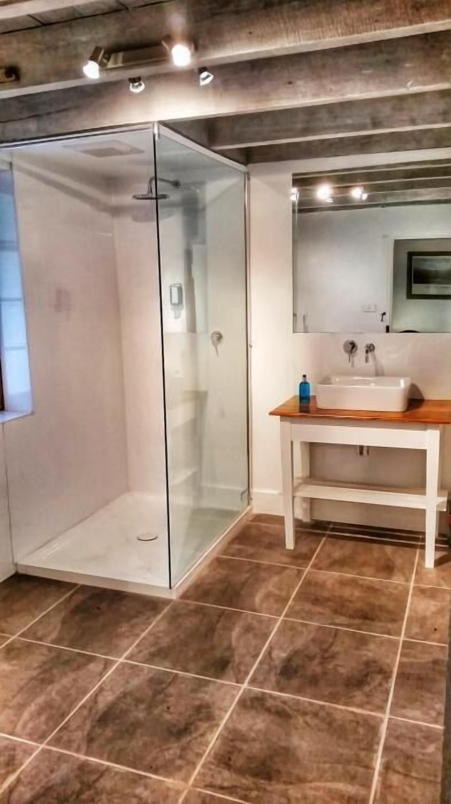 A bathroom with a glass shower enclosure, a sink with a wooden countertop, and a mirror above the sink.
