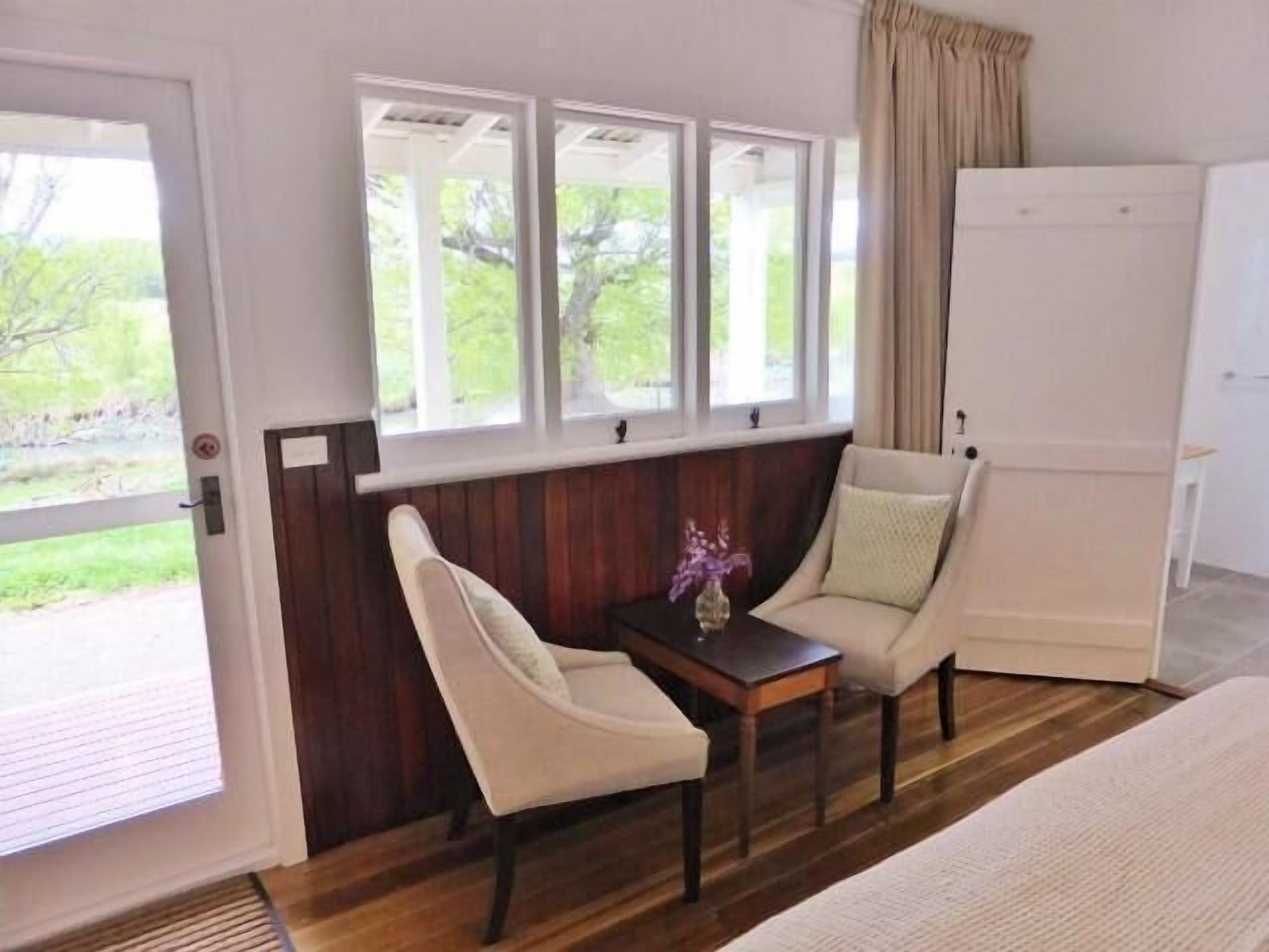 A room with a bed, a small table with a vase, two chairs, and a window with curtains.