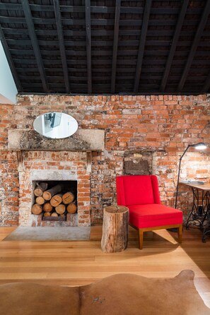 A rustic room with a brick fireplace, a red chair, and a wooden stool.