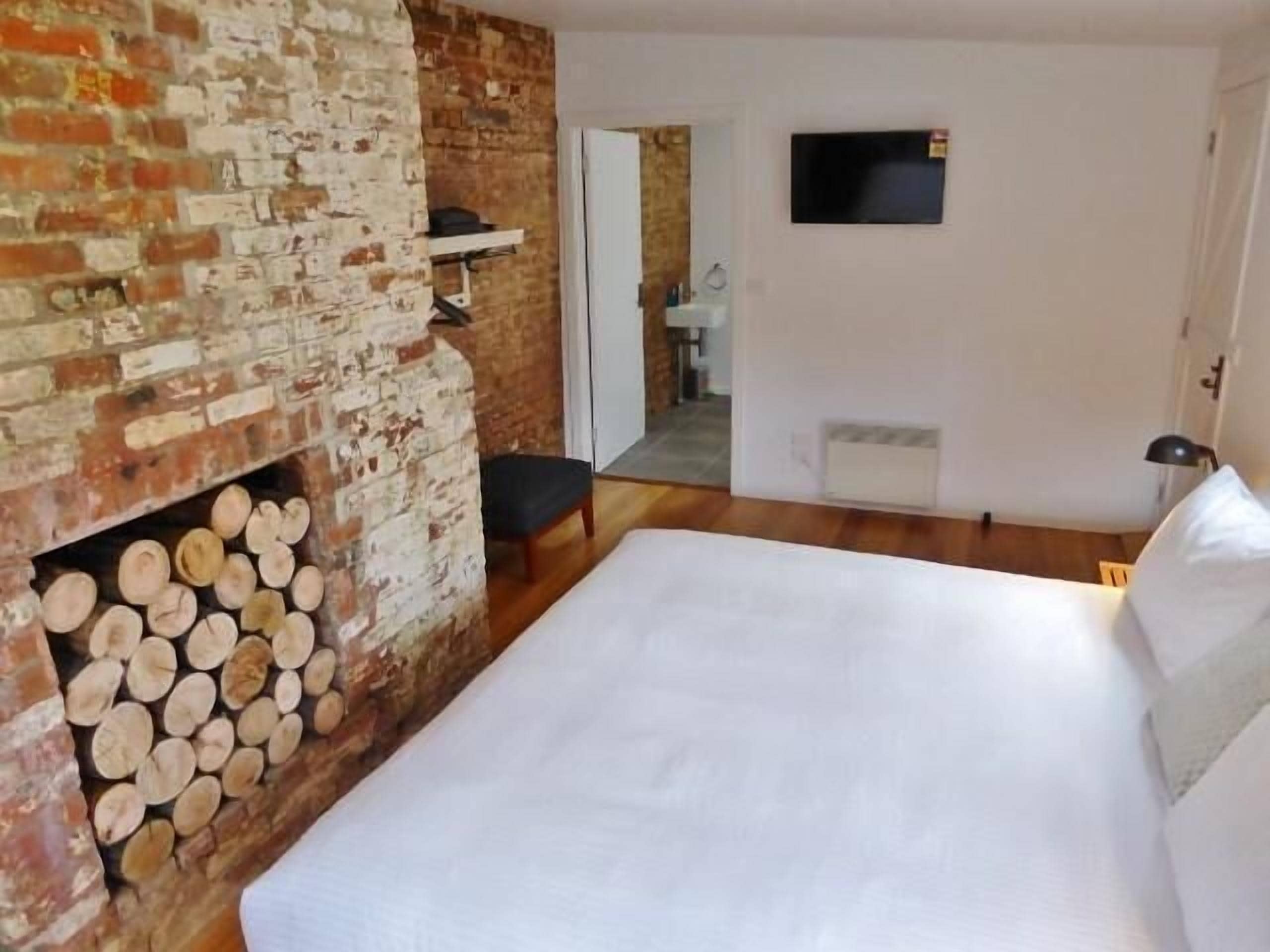 Un dormitorio con chimenea de ladrillo, una cama, un televisor y un pasillo que lleva a un baño.