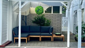 Un espace extérieur aménagé avec un coin salon abrité, comprenant un canapé de couleur sombre et des bancs en bois, une plante en pot et un luminaire décoratif suspendu.