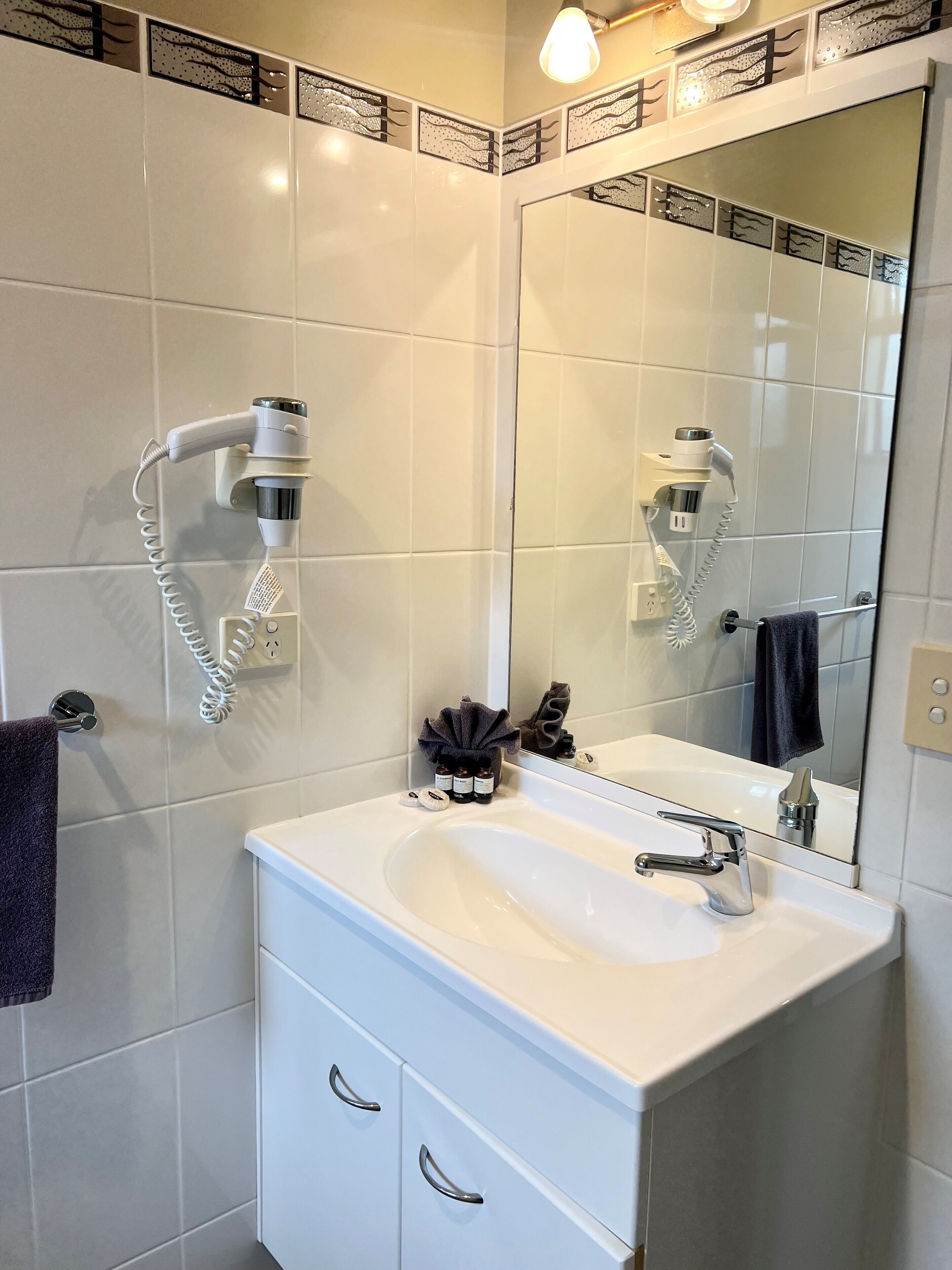 A bathroom with a white sink, a mirror, and two hair dryers mounted on the wall.