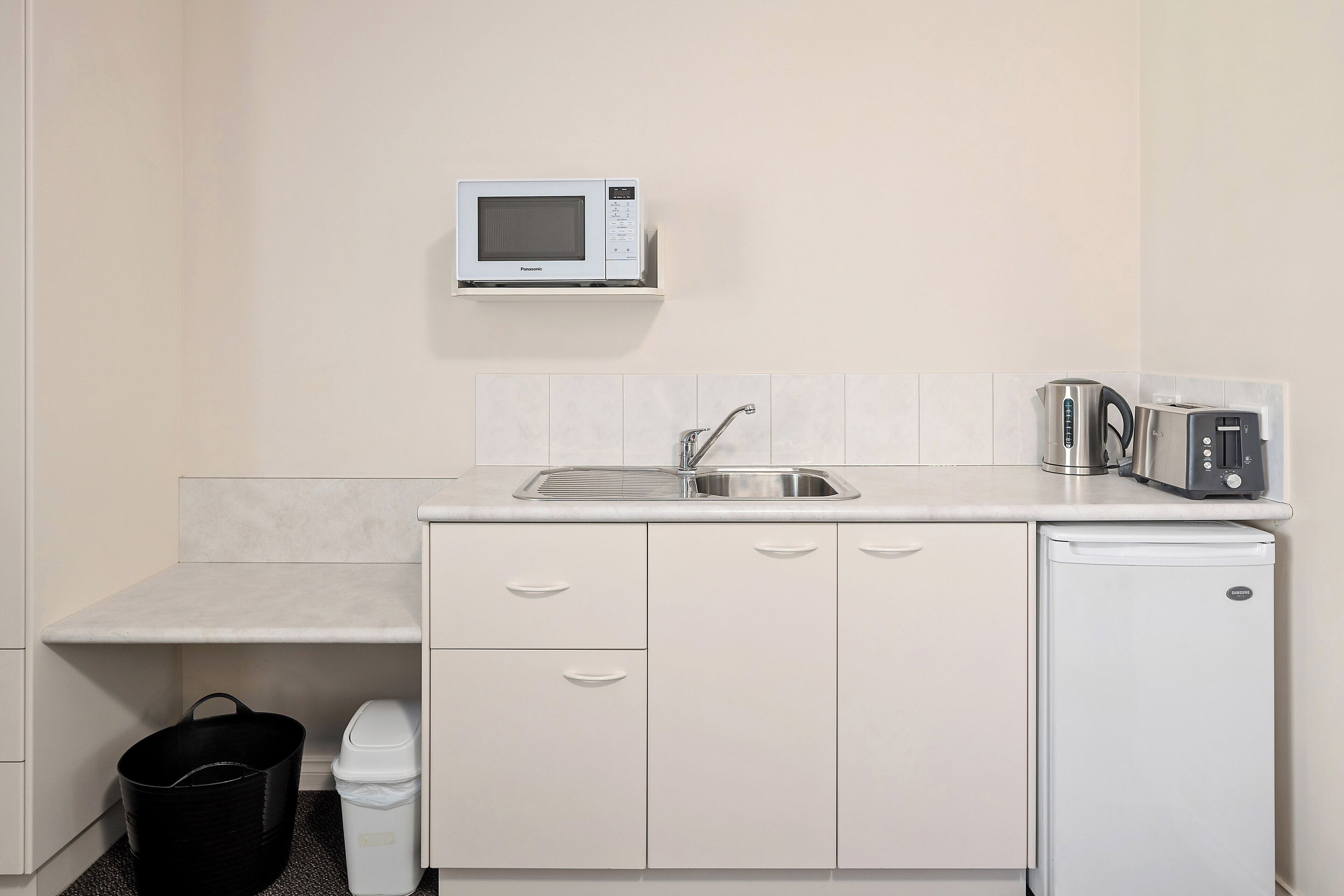 A compact kitchenette with a microwave, toaster, sink, and a small refrigerator.