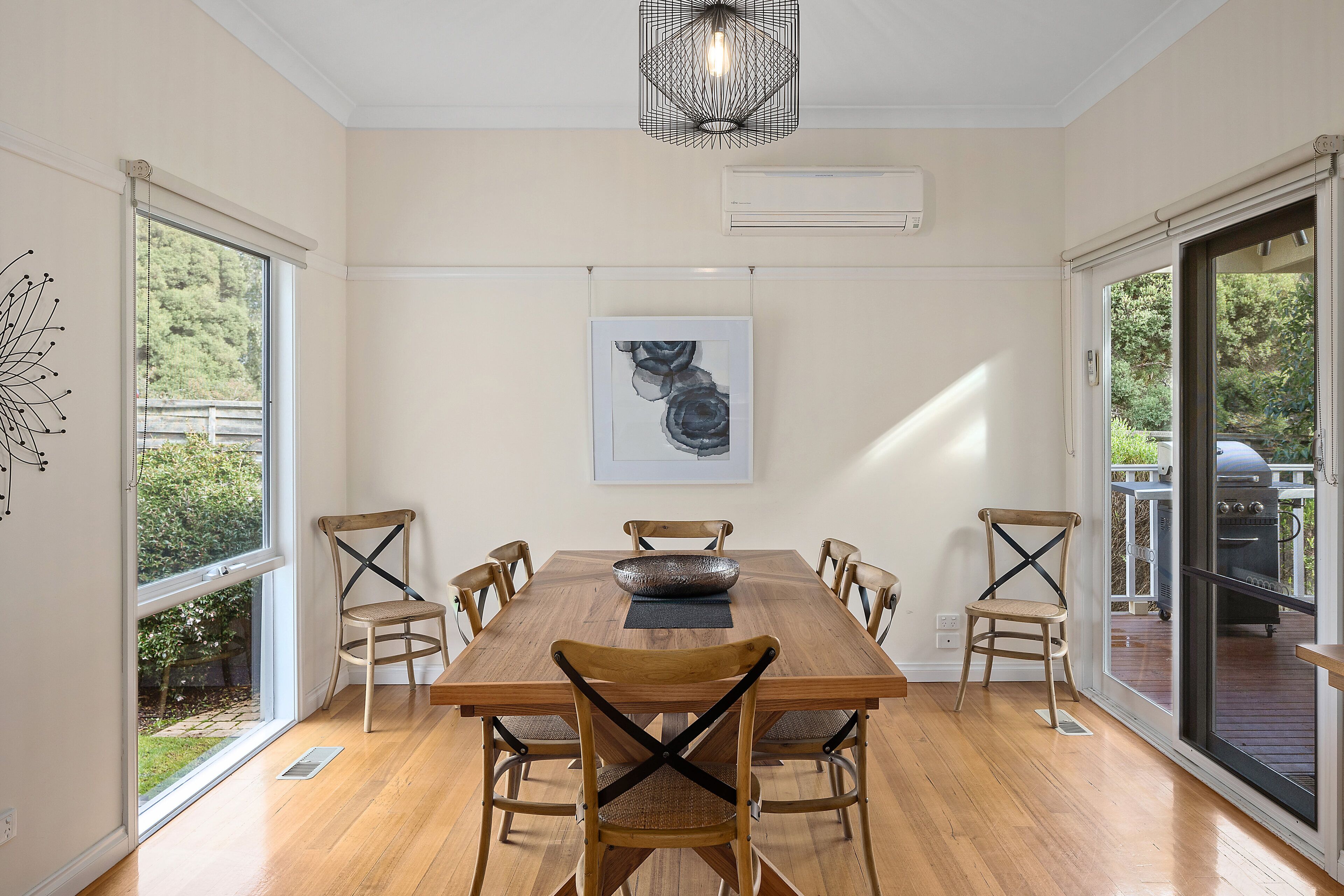 Un comedor con una mesa de madera, seis sillas, un bol negro y una obra de arte enmarcada en la pared.