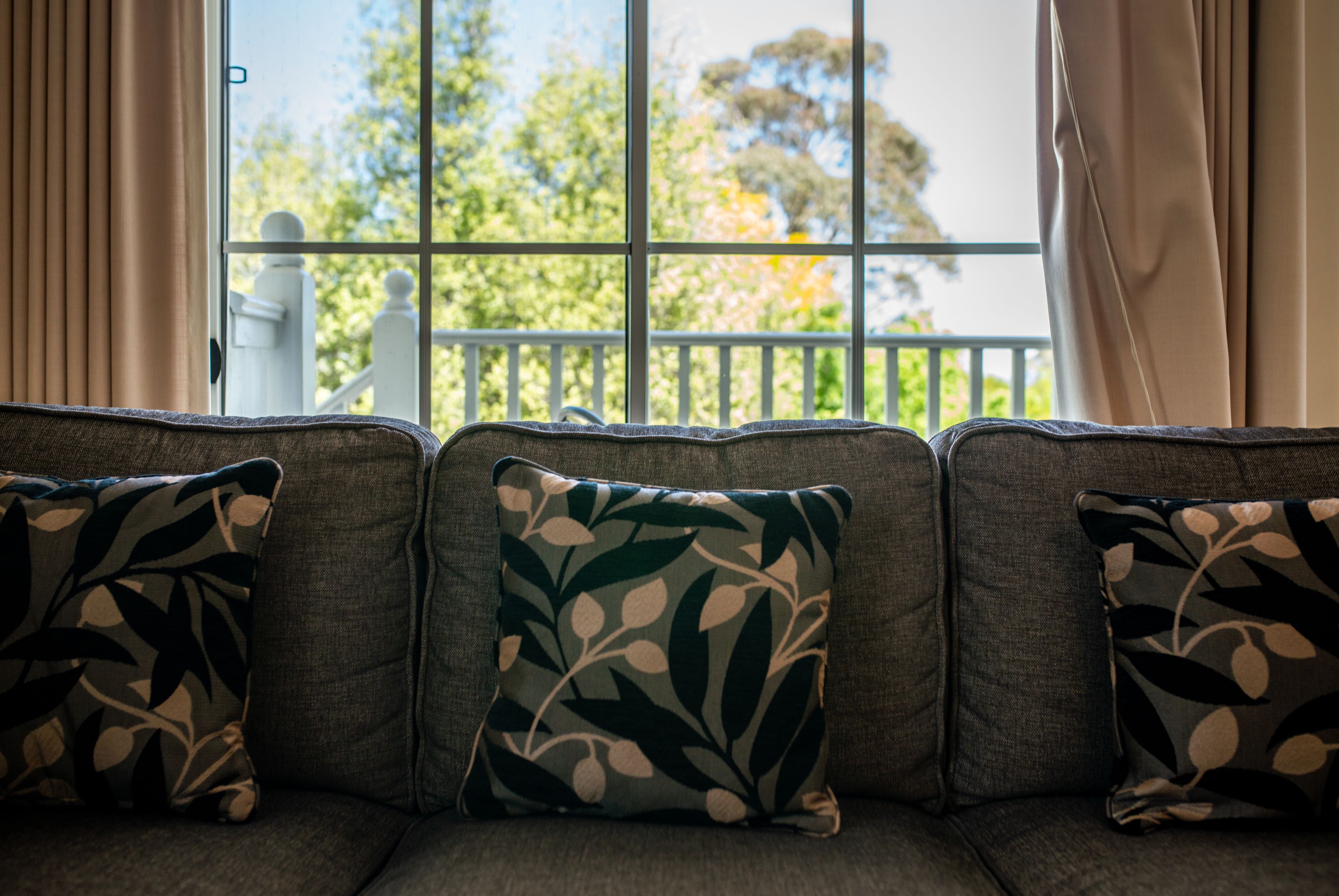 A sofa with patterned cushions and a view of a balcony with a railing.