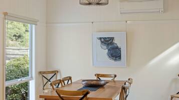 A dining area with a wooden table, six chairs, a decorative bowl, a framed artwork, and an air conditioning unit on the wall.