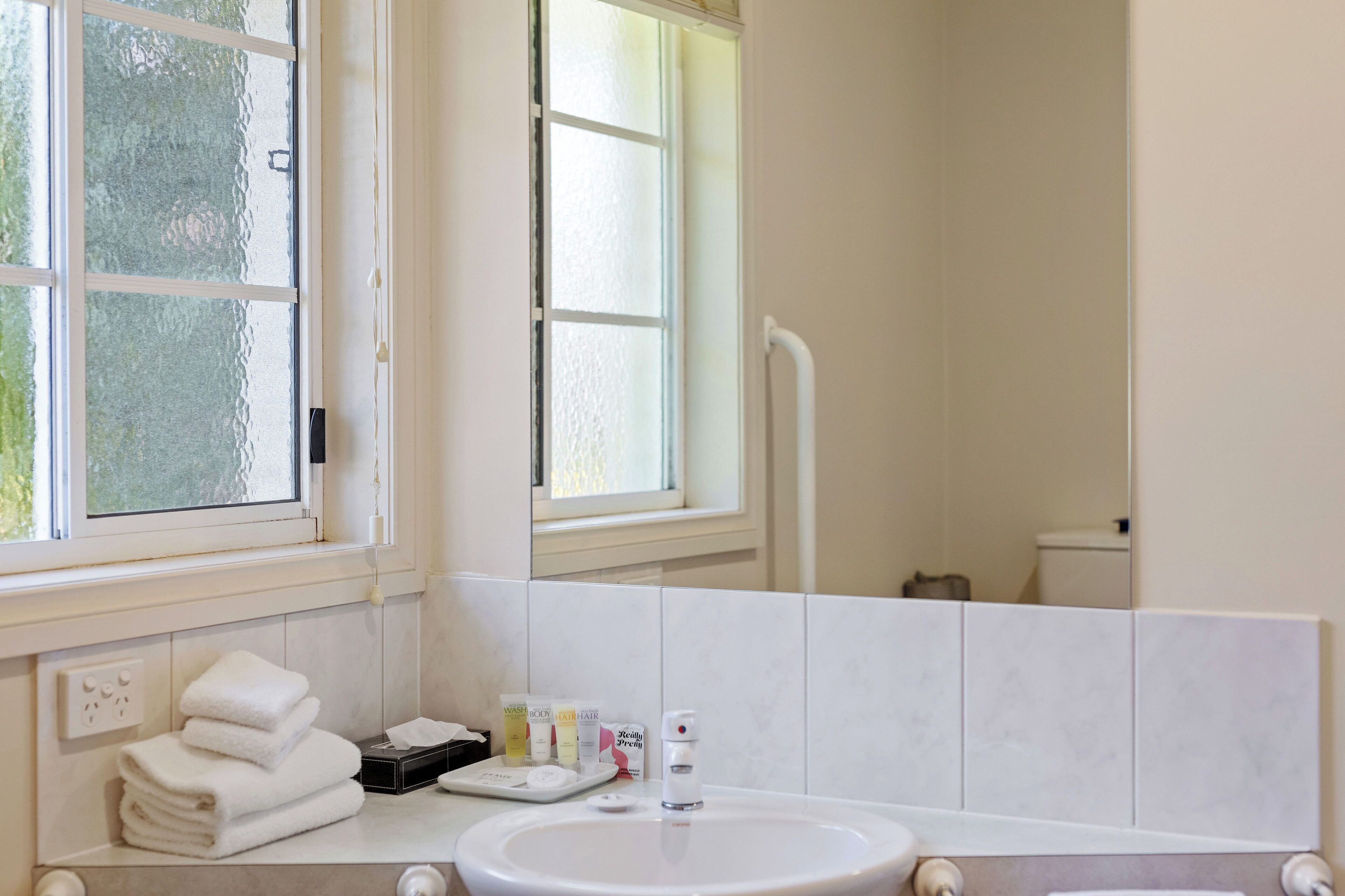 Un baño con lavamanos, artículos de aseo y ventana.