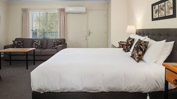 A hotel room with a large bed, a sofa, a small table, and a window with curtains.