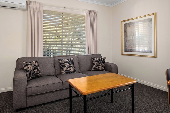 A living room with a grey sofa, two patterned pillows, a wooden coffee table, and a framed picture on the wall. - Yarra Gables (Healesville)