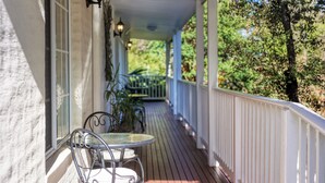 A covered porch with a table and chairs, white railings, and a view of trees. - Yarra Gables (Healesville)