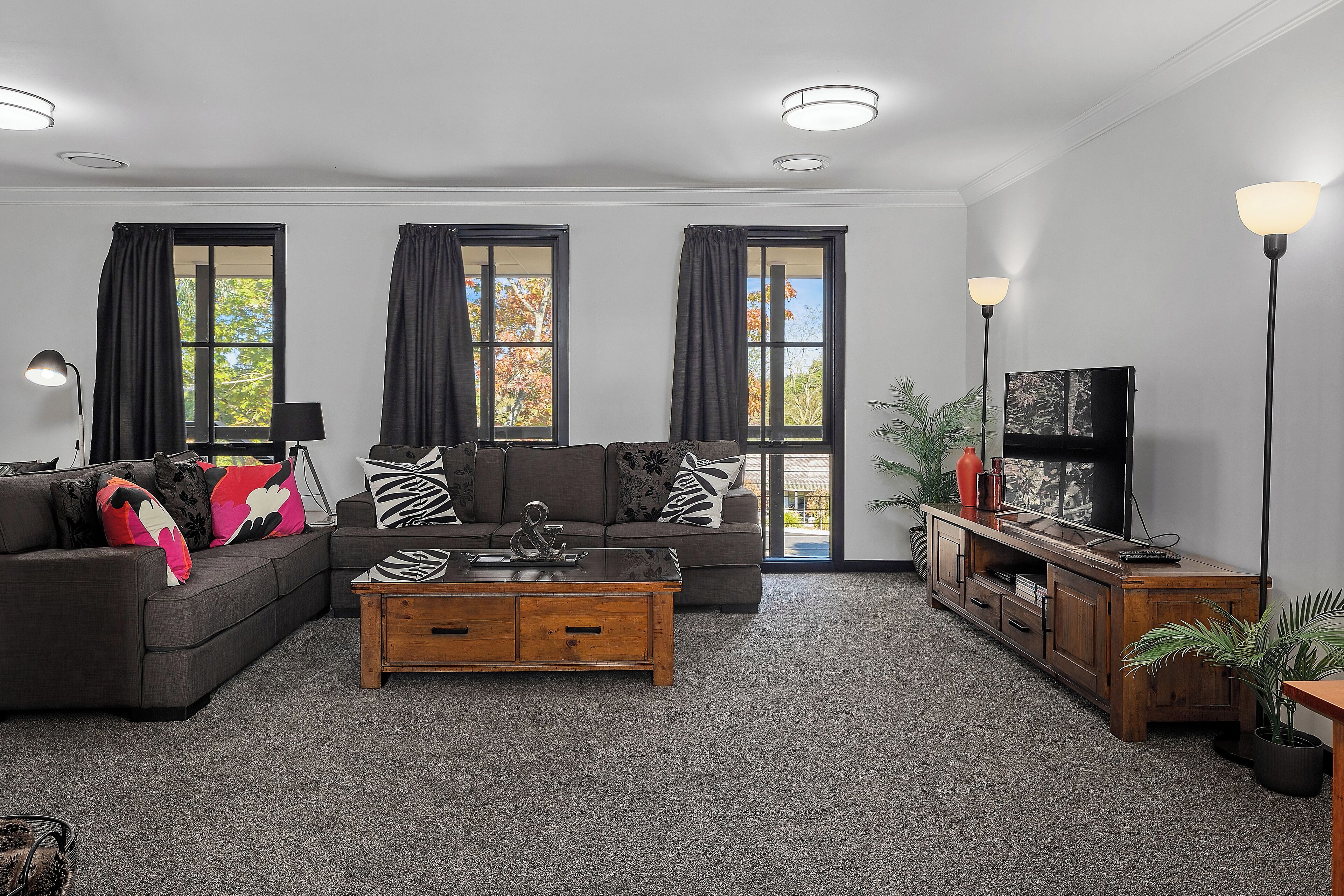 A modern living room with two sofas, a coffee table, a TV stand, and large windows with curtains.