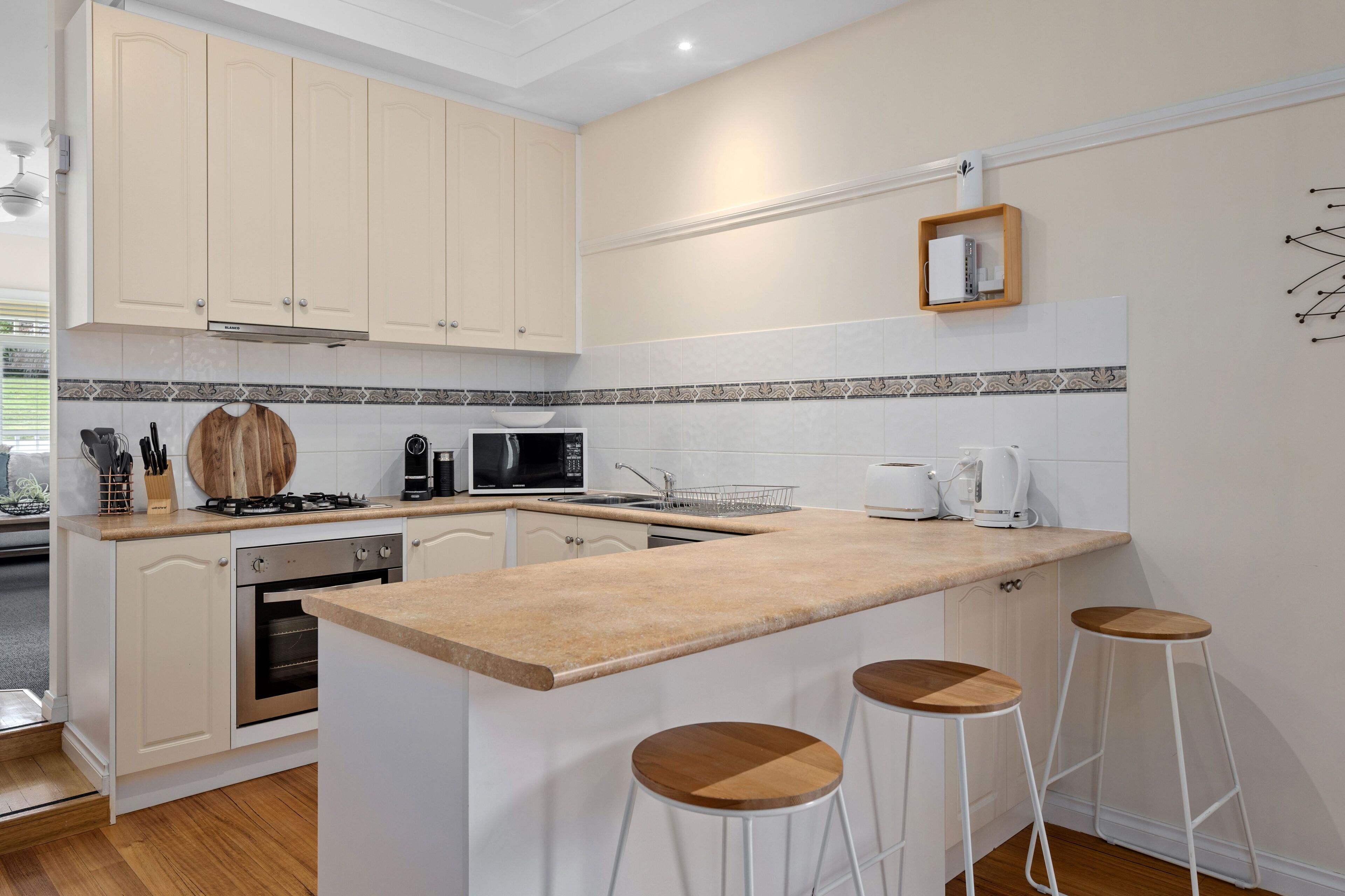 A kitchen with white cabinets, a wooden countertop, a microwave, a coffee maker, and three bar stools.