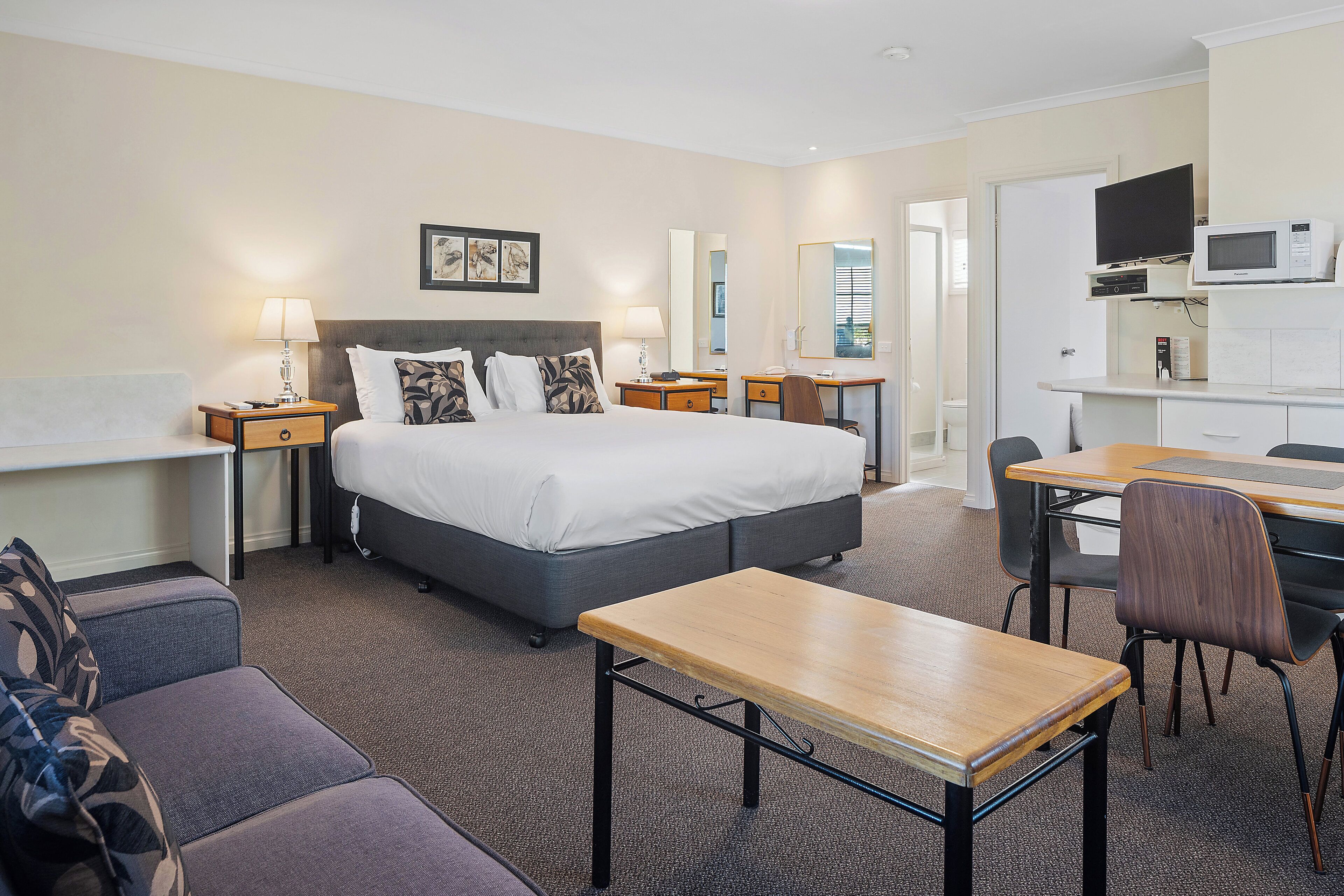 Une chambre d’hôtel comprenant un lit, des tables de chevet, un bureau, une chaise, un canapé et un téléviseur.