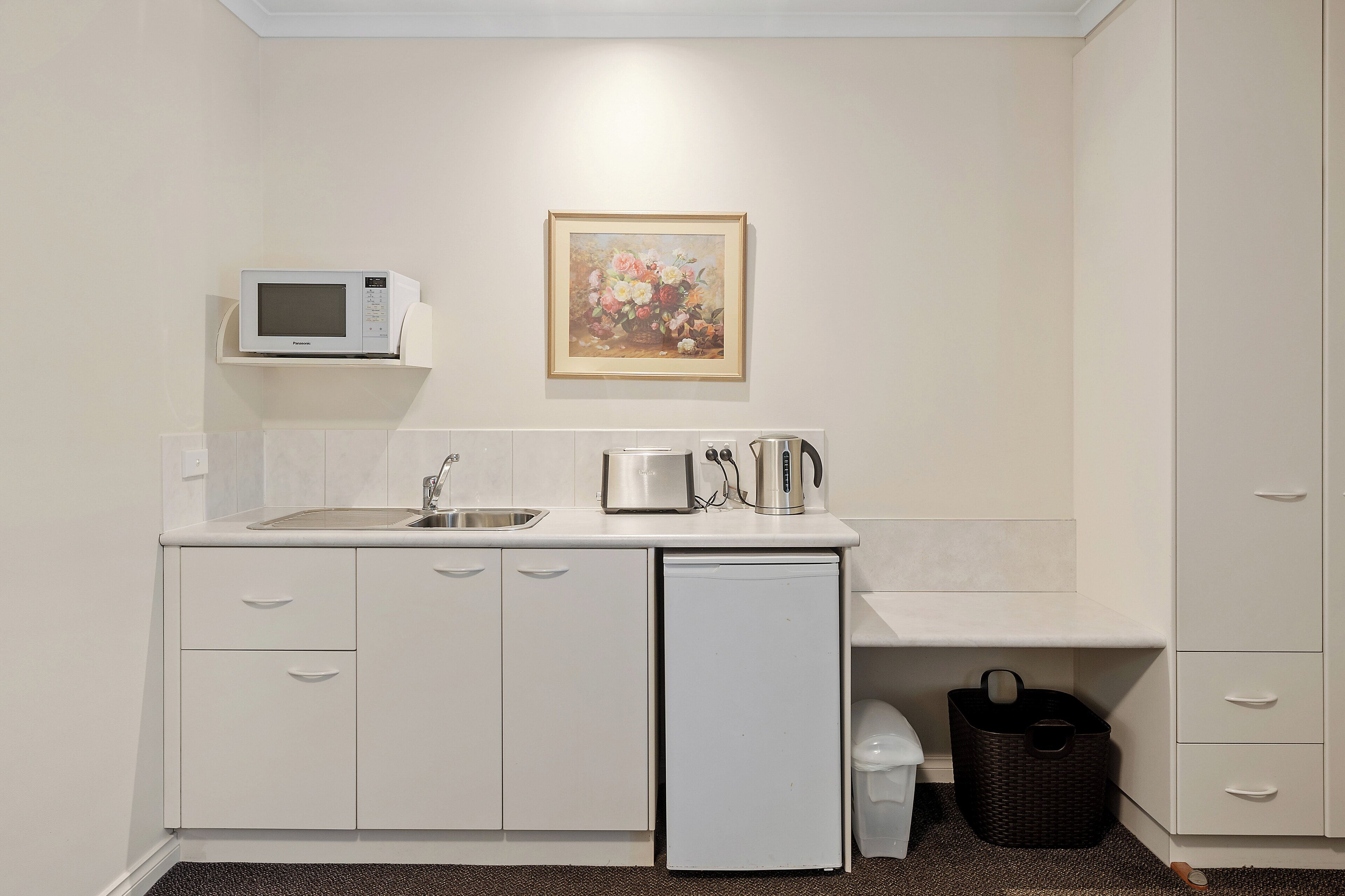A compact kitchenette with a microwave, toaster, and coffee maker on the counter, a sink, and a small refrigerator.