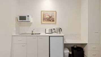 A compact kitchenette with a microwave, toaster, and coffee maker on the counter, a sink, and a small refrigerator.