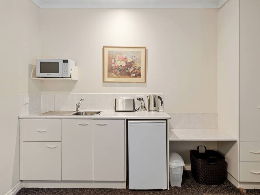 A compact kitchenette with a microwave, toaster, and coffee maker on the counter, a sink, and a small refrigerator.