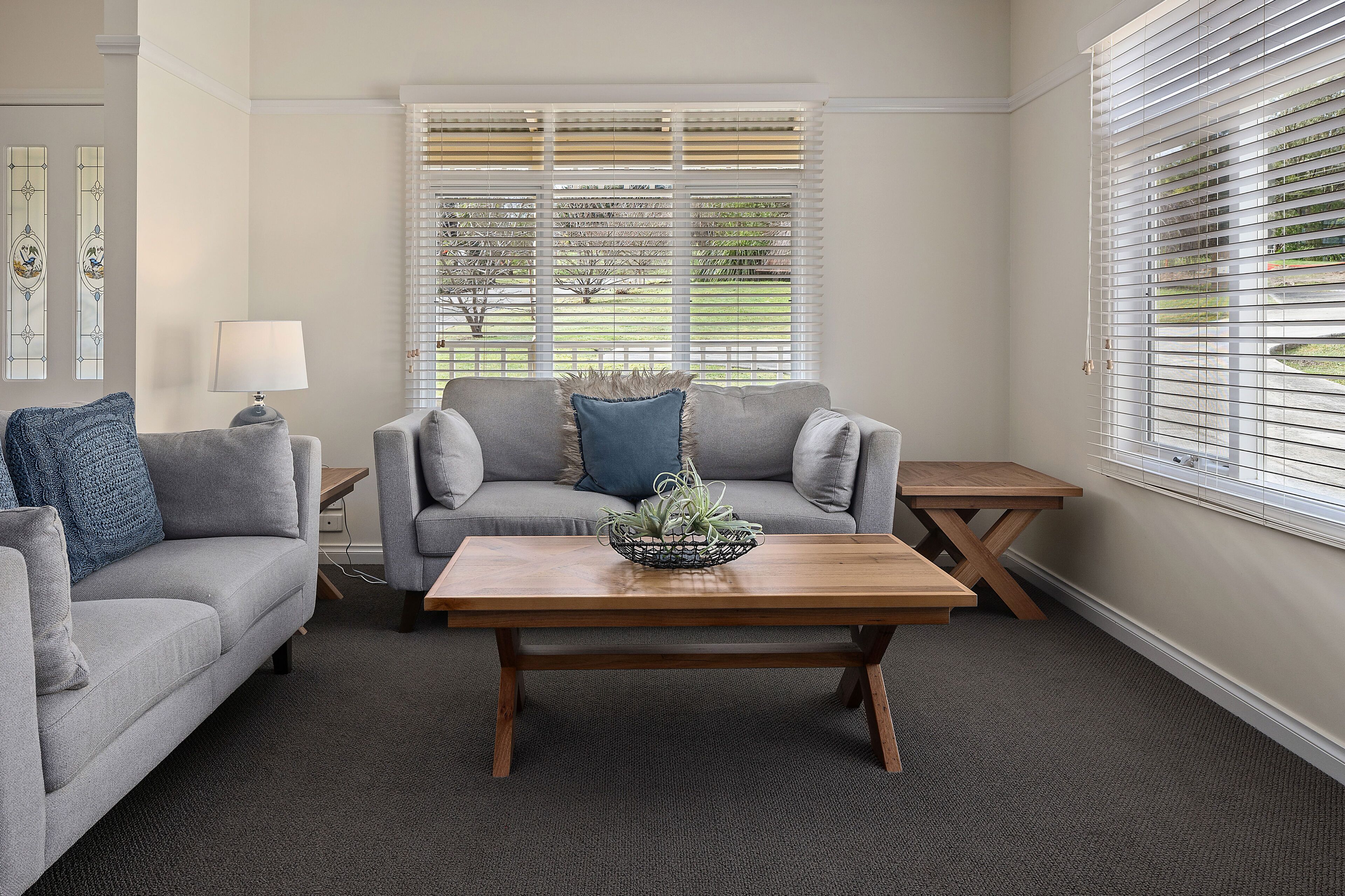 A living room with a grey sofa, a wooden coffee table with a plant, and a small wooden table.