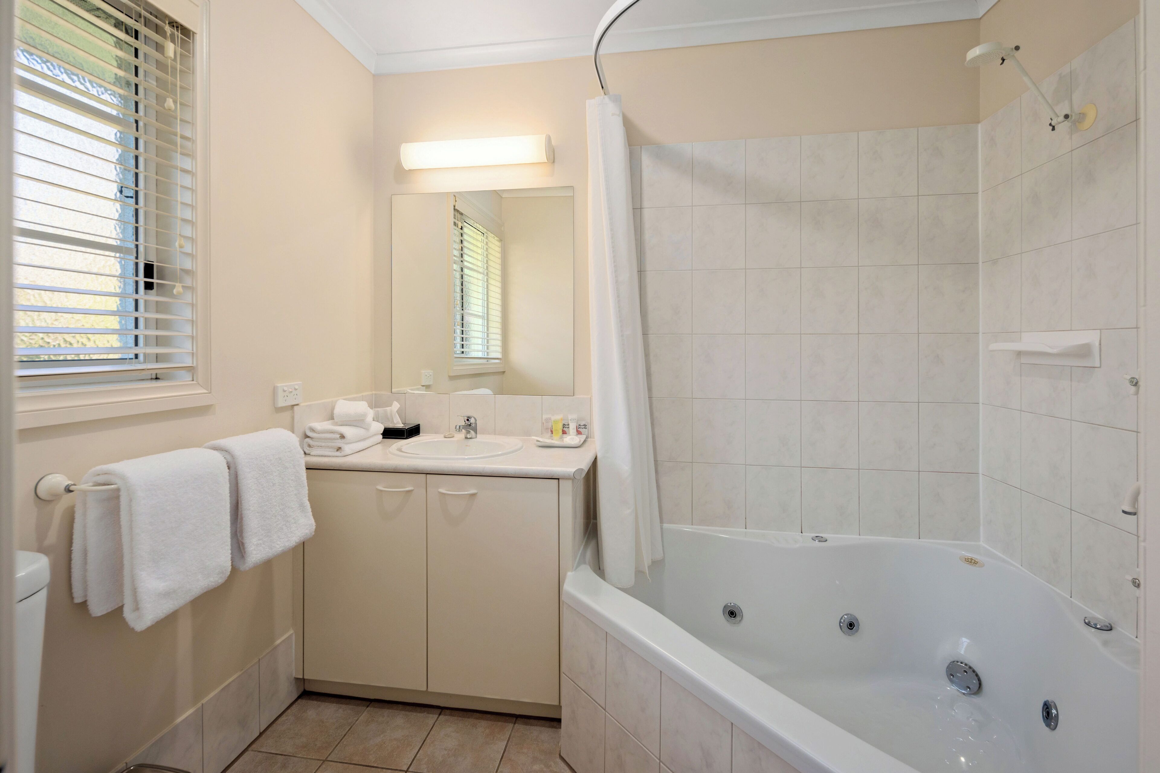 Un bagno con vasca, lavandino, specchio e finestra con persiane.