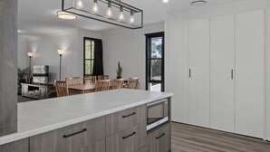 A modern kitchen with a large island, wooden cabinets, and a dining area with a table and chairs. - Yarra Gables (Healesville)