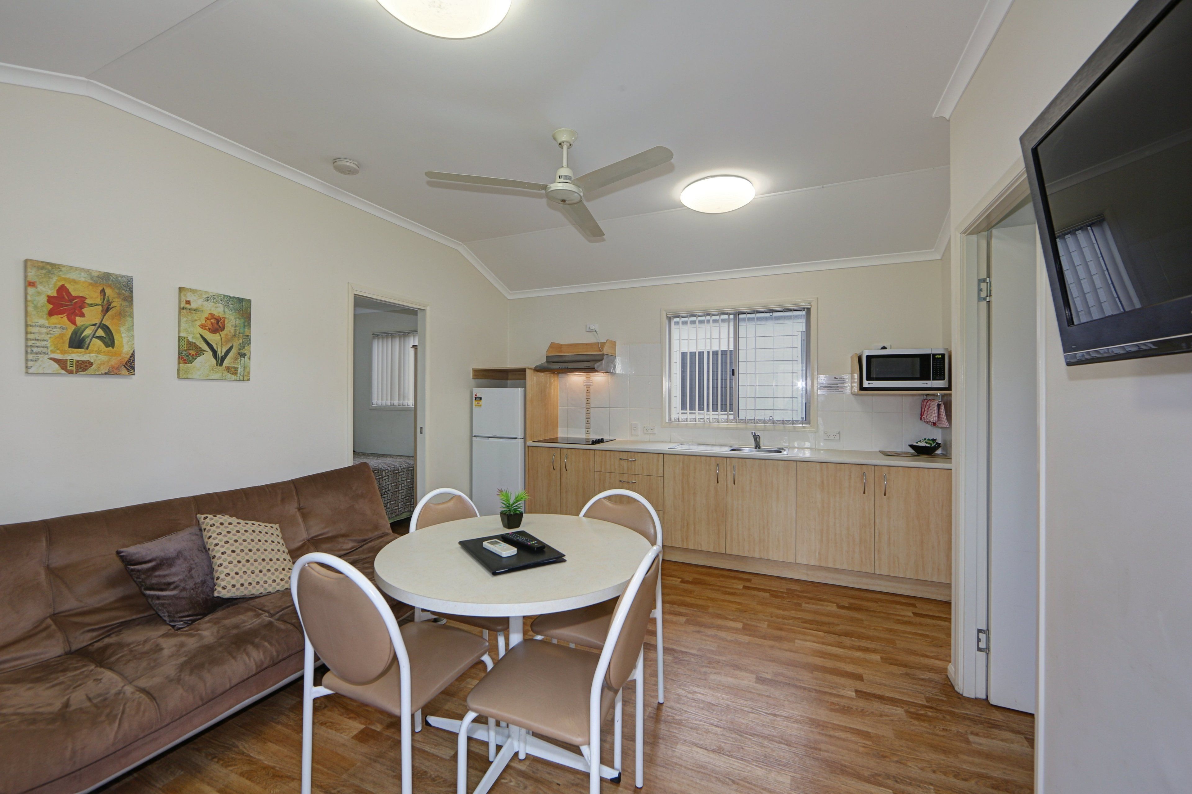 A compact living space with a kitchenette, a dining area with a round table and chairs, a brown sofa with cushions, and a ceiling fan.