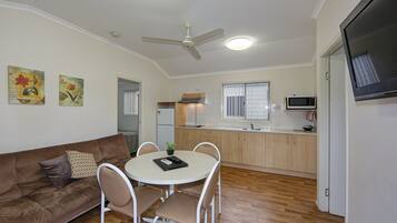 A compact living space with a kitchenette, a dining area with a round table and chairs, a brown sofa with cushions, and a ceiling fan.