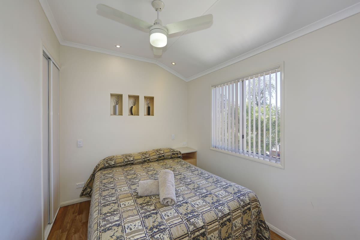 A bedroom with a bed, a ceiling fan, a window with blinds, and a door.