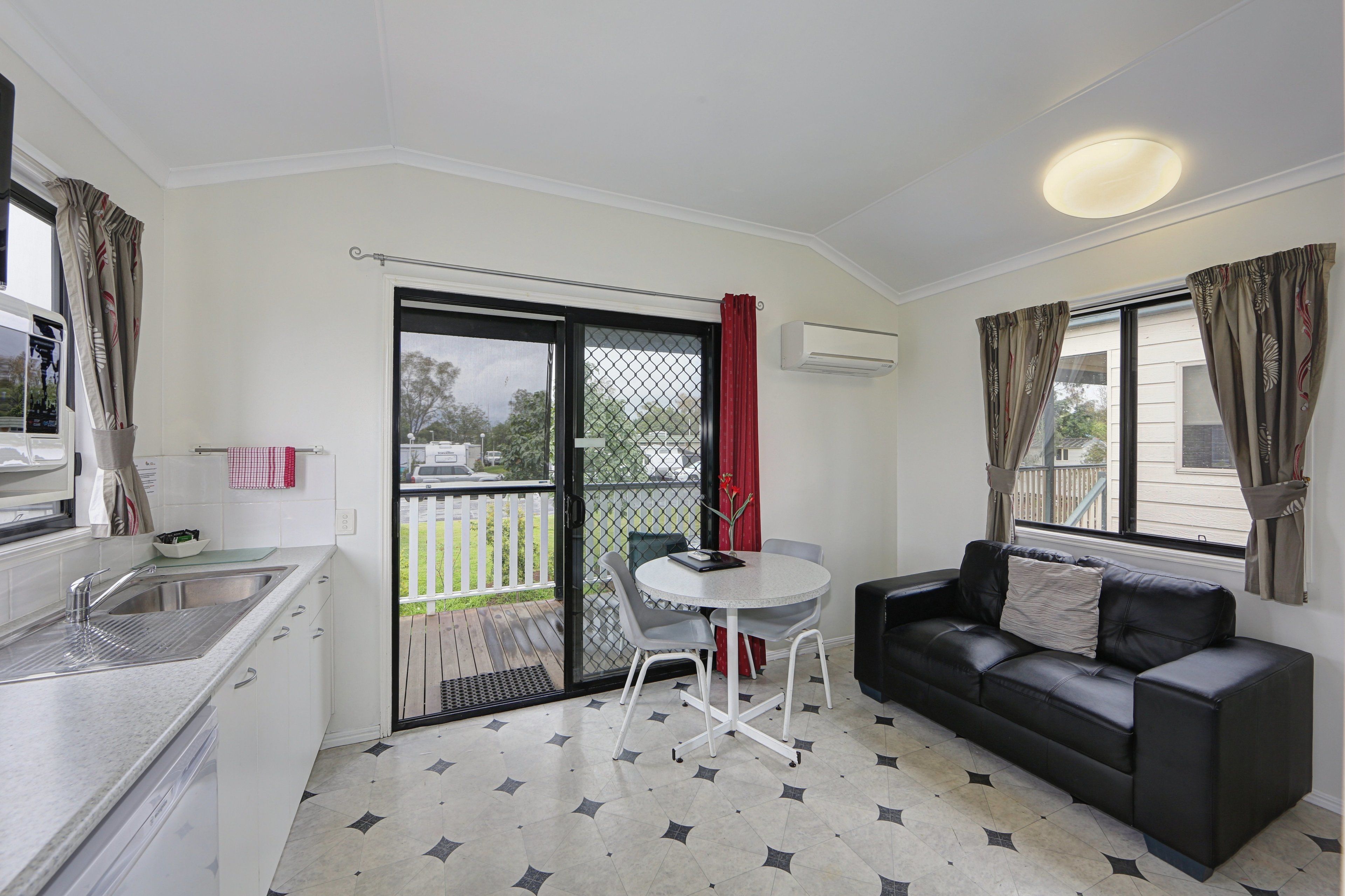 A compact kitchen with a sink, a dining area with a table and chairs, a black leather sofa, and a sliding glass door leading to a balcony.