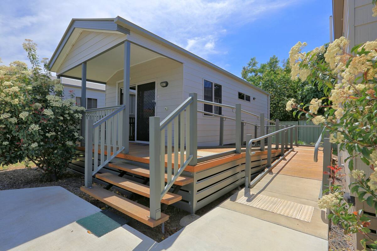 A mobile home with a covered porch, wooden steps, and a small outdoor deck.