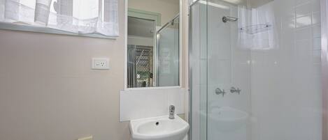 A bathroom with a glass shower enclosure, a sink, and a mirror.