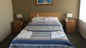 Quarto de hotel com cama, duas mesas de cabeceira, um quadro na parede e uma janela.