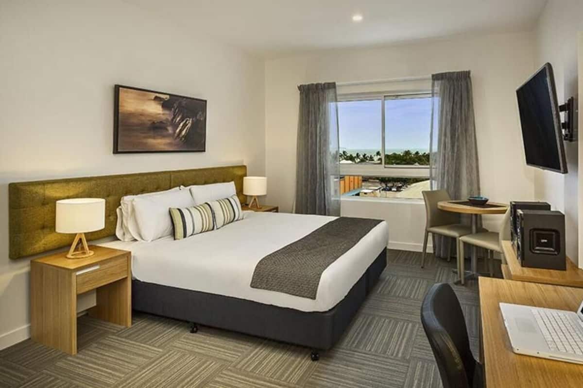 Ein Hotelzimmer mit Bett, Nachttischen, Schreibtisch, Stuhl, Fernseher und einem Fenster mit Aussicht.